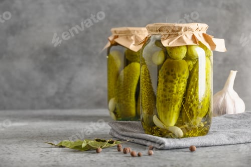 Preview: Canned vegetables cucumber in glass jars on grey background.