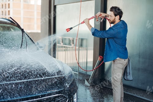 Preview: Young man washing car at self service car wash