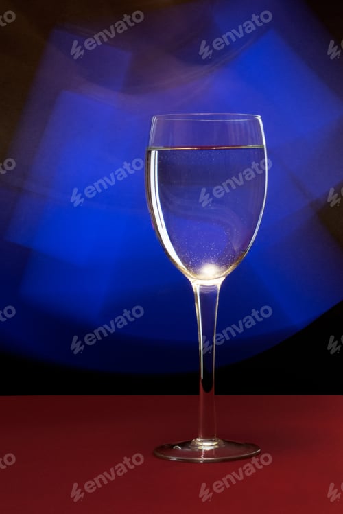 Preview: Vertical closeup of water in a wine glass against a blue neon light in a studio