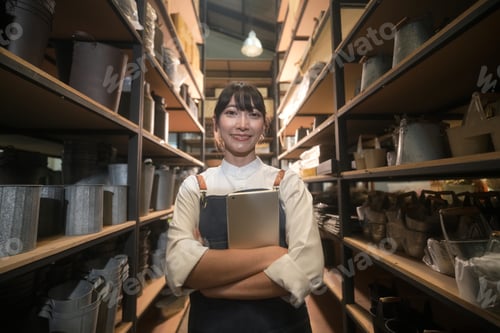 Preview: Smiling woman in apron holding tablet in a storage room with shelves full of containers