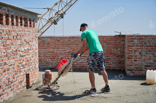 Preview: Male worker using power trowel machine at construction site.