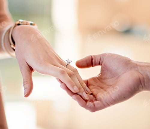 Preview: Closeup shot of a man putting an engagement ring onto his fiancees finger