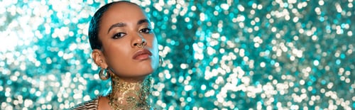 Preview: african american woman with piercing and gold on neck posing on sparkling blue background, banner