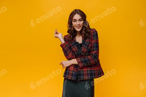 Preview: Wonderful brunette girl in striped jacket and black dress smiling on yellow background. Curly lady