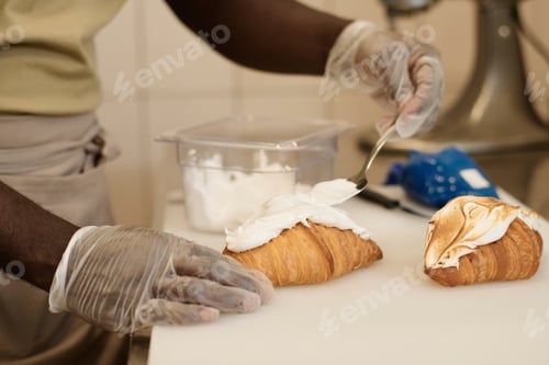 Preview: Male baker decorating fresh croissants with cream in artisan bakery