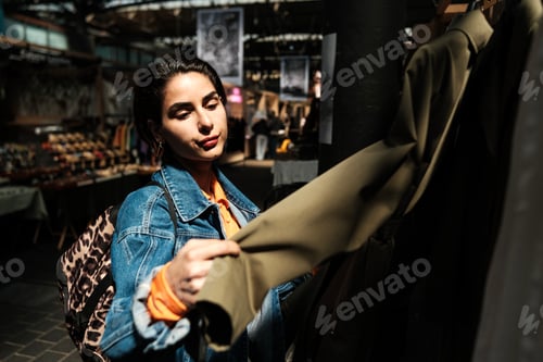 Preview: Young woman choosing clothes in vintage shop at flea market