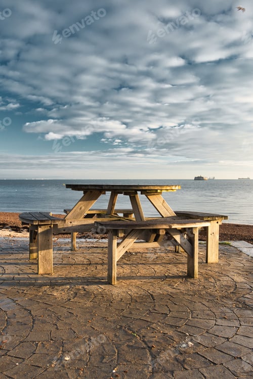 Preview: Wooden picnic table on the seashore, with white clouds scattered in the sky