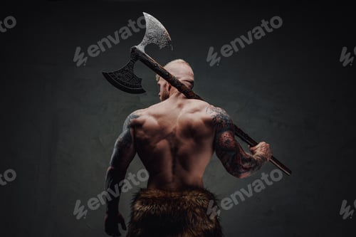 Preview: Rear view of healthy tattoed warrior in fur with axe on a dark background