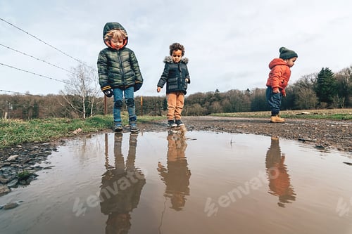 Preview: Three young children play outdoors in the winter, jumping in puddles along a dirt road