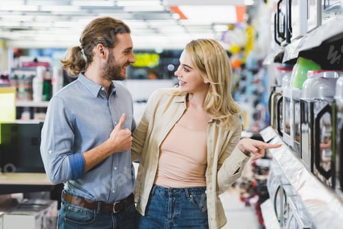 Preview: smiling consultant showing like and woman pointing with finger at microwave in home appliance store