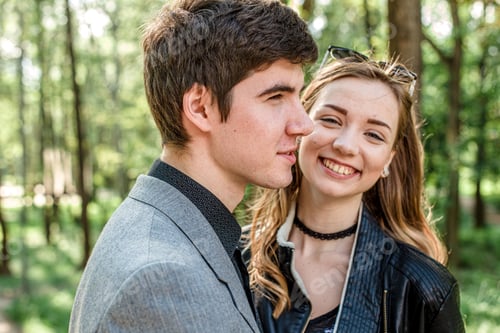 Preview: Happy young girl laughing happily while standing next to her beloved boyfriend in spring in the park