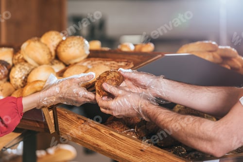 Preview: cropped shot of shop assistant giving loaf of bread to woman in supermarket