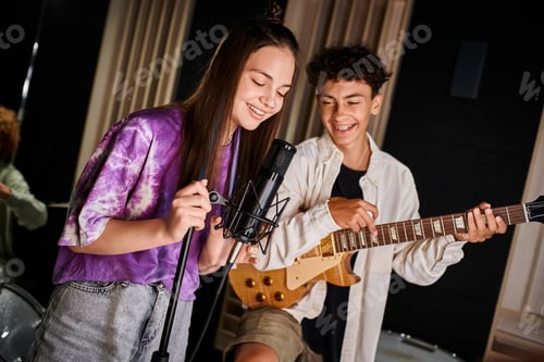 Visualização: adorável adolescente alegre cantando música ao lado de sua amiga com aparelho ortodôntico tocando guitarra no estúdio