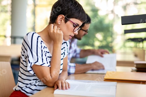 Preview: Exhausted young female studying and preparing for exam in college library. Education people concept
