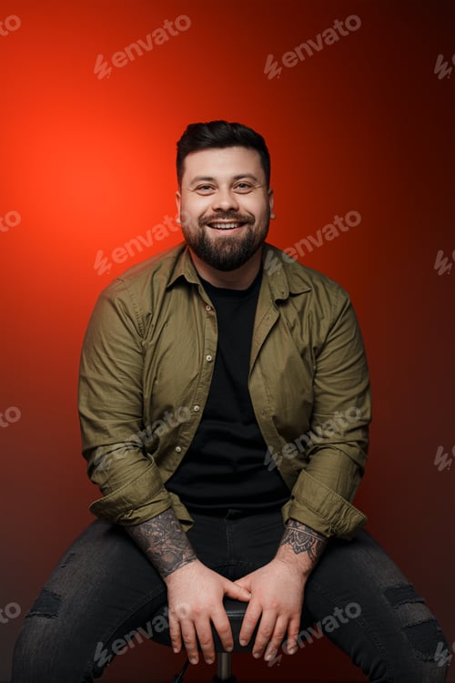 Preview: Cheerful bearded man with tattoo against red background