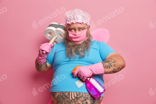 Preview: Serious childish man wears shower cap, protective mask, undersized t shirt, rubber gloves, goes to y