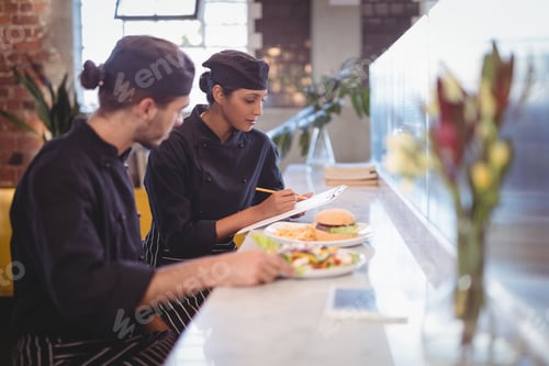 Preview: Young wait staff sitting with clipboard and food at counter