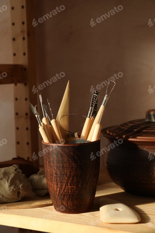 Preview: Set of different crafting tools and clay dishes on wooden table in workshop