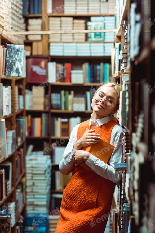Preview: beautiful and blonde woman with closed eyes in glasses holding book in library