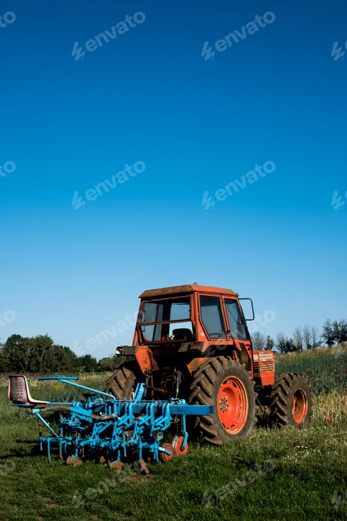 Preview: Red tractor with blue harrow on a farm.