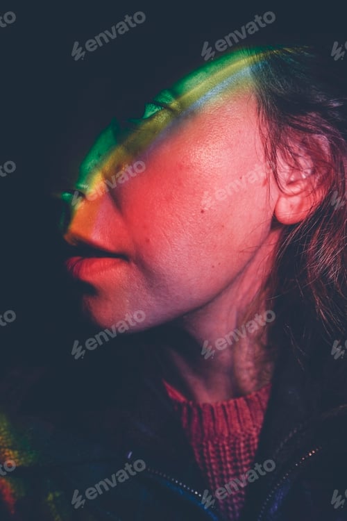 Preview: Artistic portrait of a young woman illuminated by colored lights in the dark