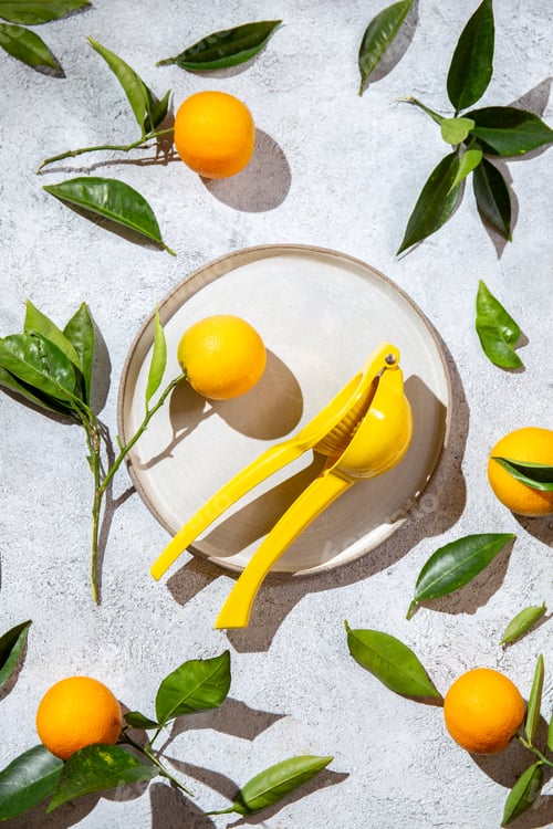 Preview: Whole oranges with orange tree leaves around plate and juicer top view, flat lay, summer and healthy