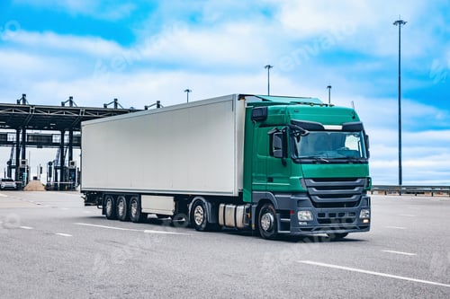 Preview: A Green Freight Truck Approaches a Distribution Center with Long Clouds and Overcast Sky
