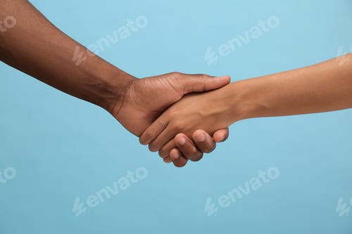 Preview: Woman and African American man shaking hands on light blue background, closeup