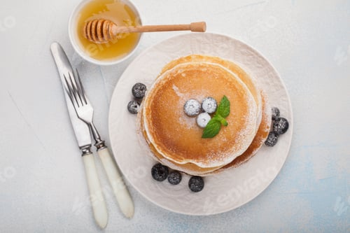 Preview: A stack of delicious pancakes with honey and blueberries on a light blue background.