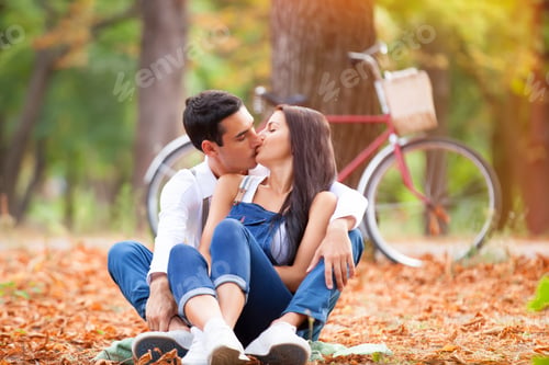 Preview: Teen couple with retro bike kissing in the park in autumn time