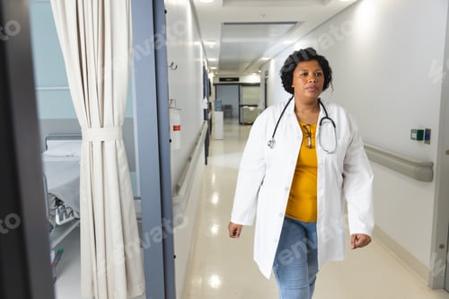 Preview: African american female doctor wearing lab coat and stethoscope walking in corridor at hospital