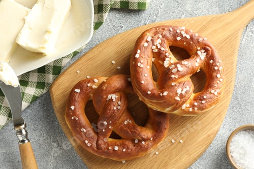 Preview: Tasty pretzels with salt and butter on light grey table, flat lay