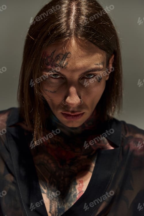 Preview: portrait of young stylish man with tattoos on face looking straight at camera, fashion concept
