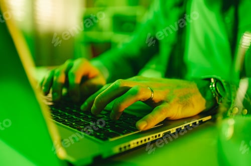 Preview: Close-up of a programmer typing code on a laptop from a green-lighted room.