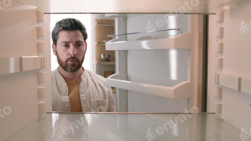 Preview: Hungry Caucasian bachelor man looking for food in empty fridge finding no meal products feeling sad