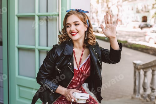 Preview: Joyful lady in leather jacket sitting near door in cafe with instant camera in hand happily
