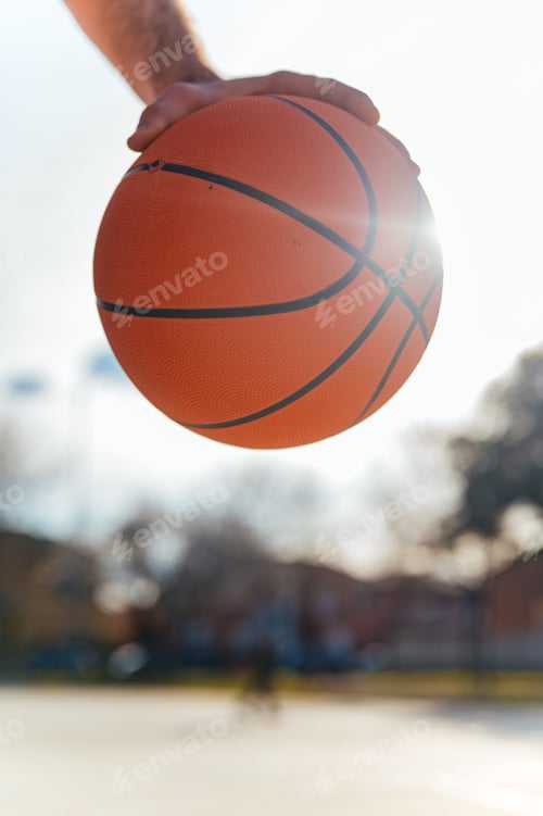 Preview: Hand holding basketball ball in street court on sunny day