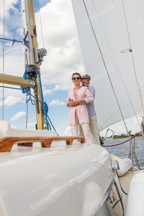 Preview: sailor man in a cap with a girl on a boat under sail against the sky and water