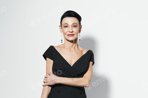 Preview: Confident woman in elegant black dress posing with hands on hips in front of white wall