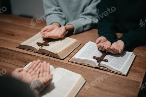 Preview: Group of Christians sit together and pray around a wooden table with blurred open Bible pages
