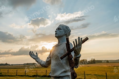 Preview: Statue with cross at sunset in field