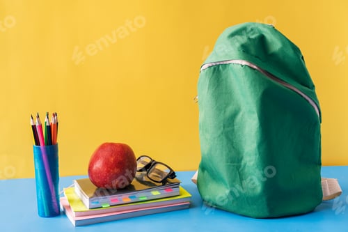 Visualização: Material escolar e mochila verde sobre fundo azul