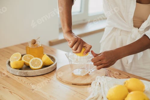 Preview: Young woman cooking homemade lemonade using juicer and fresh lemons on a kitchen.