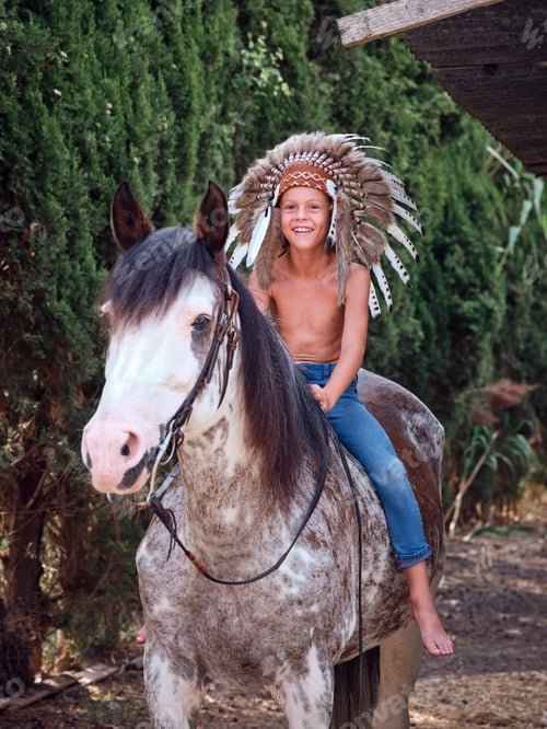 Preview: Cheerful boy in war bonnet riding gray horse