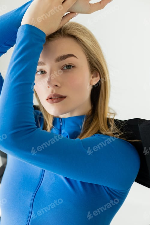 Preview: portrait of blonde woman in blue long sleeve shirt posing with raised hands isolated on grey