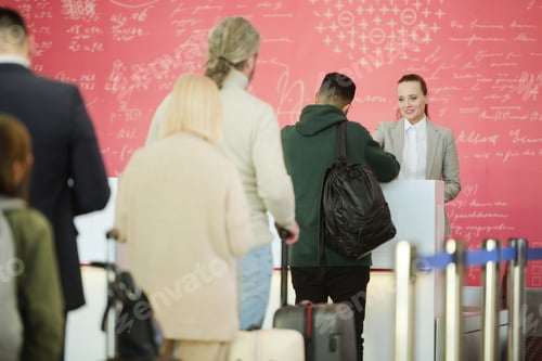 Preview: Young pretty female receptionist standing by counter and checking documents of male passenger