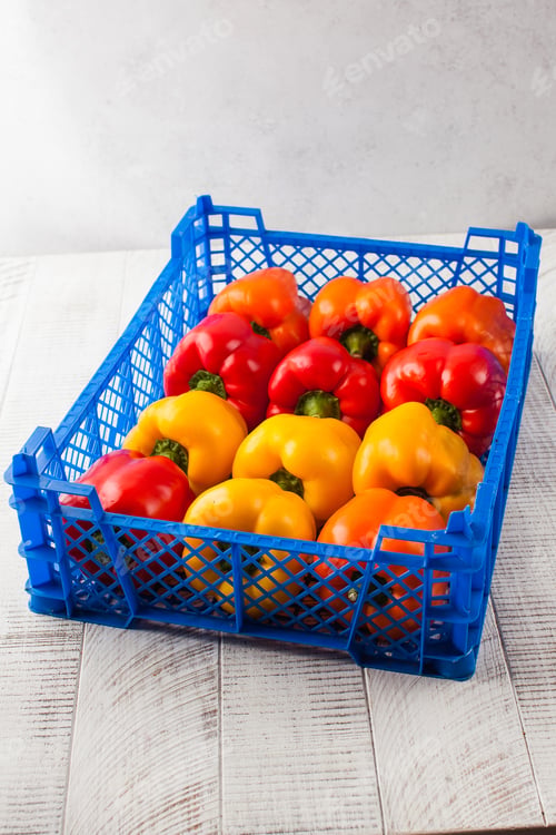 Preview: Multicolored ripe sweet pepper in a plastic box on a light wooden background. Vegetables.