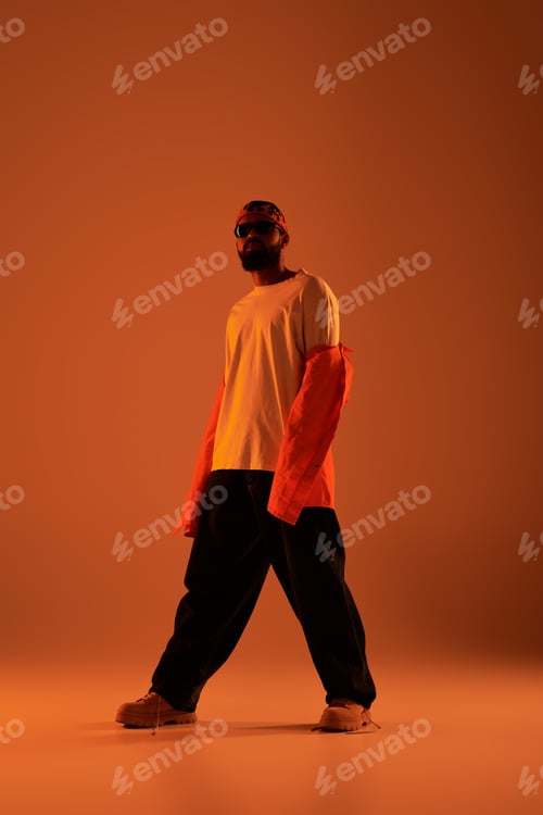Preview: Handsome man in stylish summer outfit poses confidently in warm orange light setup