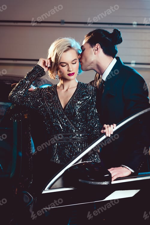 Preview: stylish man kissing beautiful seductive woman near car