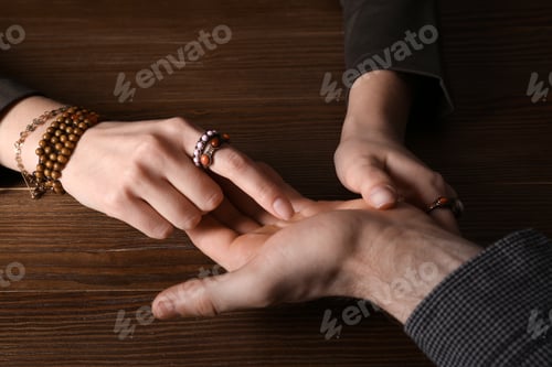 Preview: Chiromancer reading lines on man's palm at table, closeup
